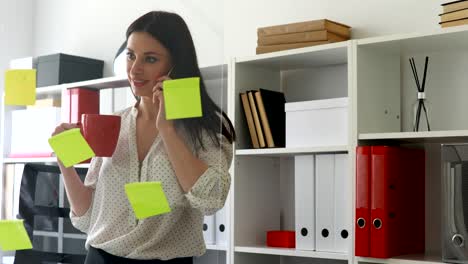 businesswoman in white blouse considering stickers on glass and talking on phone