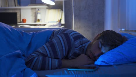 Phone-addicted-young-man-checking-his-phone-even-in-his-sleep.