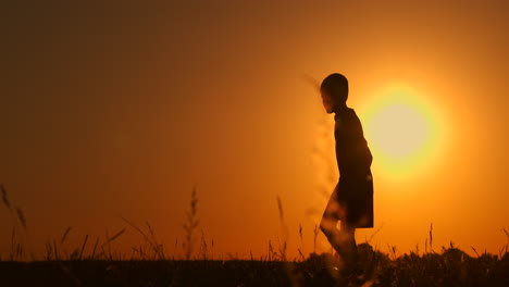 Silhouette-Eines-Jungen,-Der-Am-Strand-Football-Oder-Fußball-Spielt,-Mit-Wunderschönem-Sonnenuntergang-Im-Hintergrund,-Sportliches-Lifestyle-Konzept-Für-Die-Gelassenheit-Der-Kindheit.