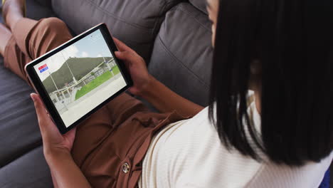 compuesto de una mujer sentada en casa en el sofá viendo un evento de salto de altura de atletismo en una tableta