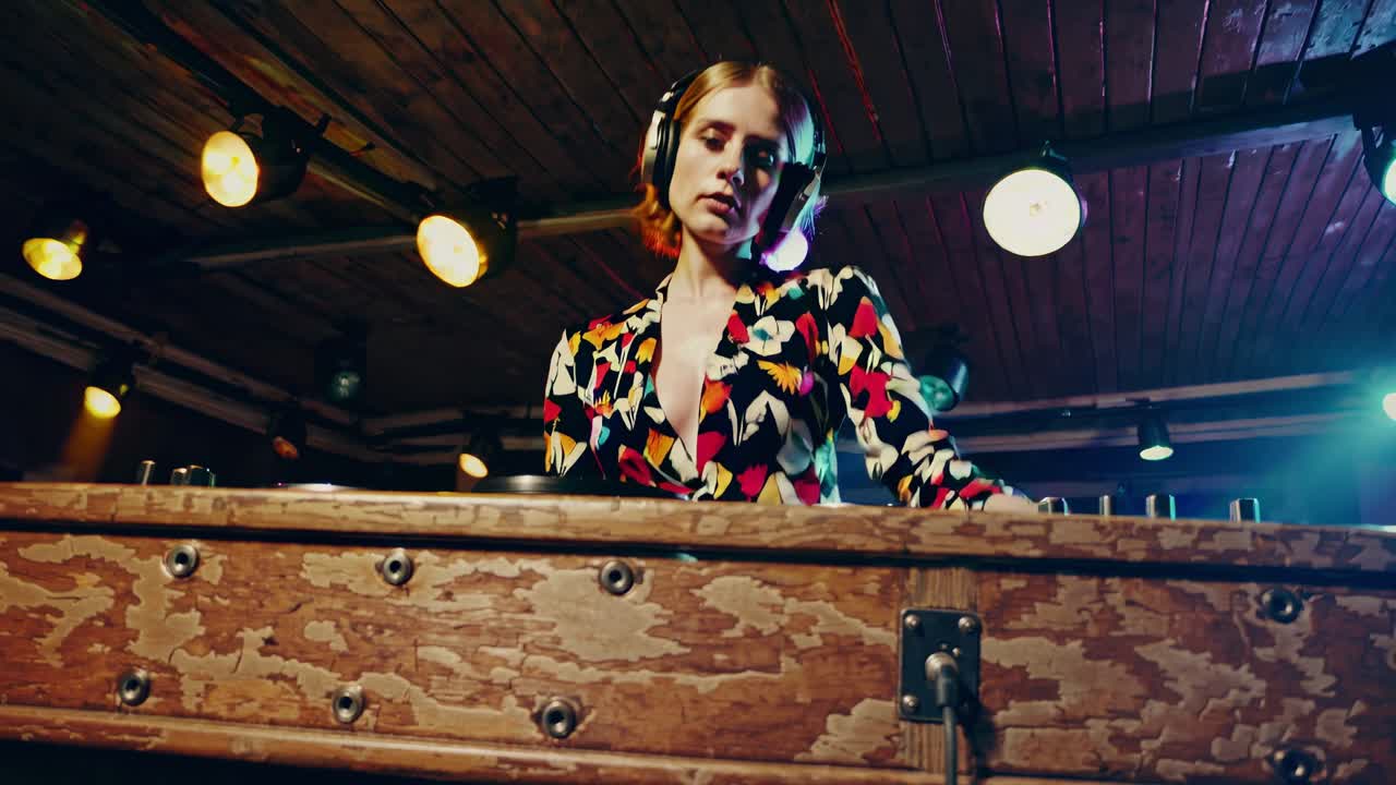 Confident female DJ wearing headphones, mixing music on a turntable at a vibrant nightclub, energizing the crowd with electrifying beats under a dazzling display of colorful lights