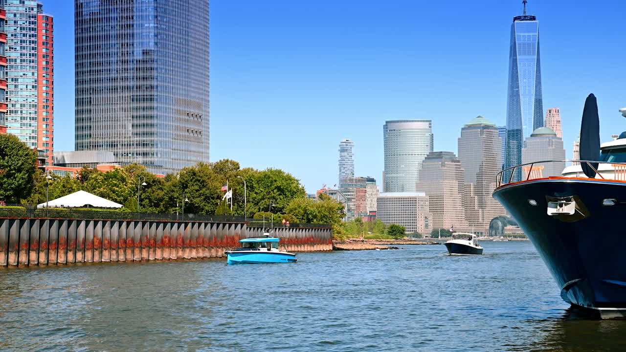 Diverse boats move by the riverscape along the waterfront. High-rises and skyscrapers of Manhattan at backdrop