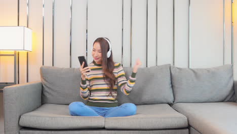 Girl-on-couch-with-Phone-and-Headphones-Listening-to-Music-and-Dancing