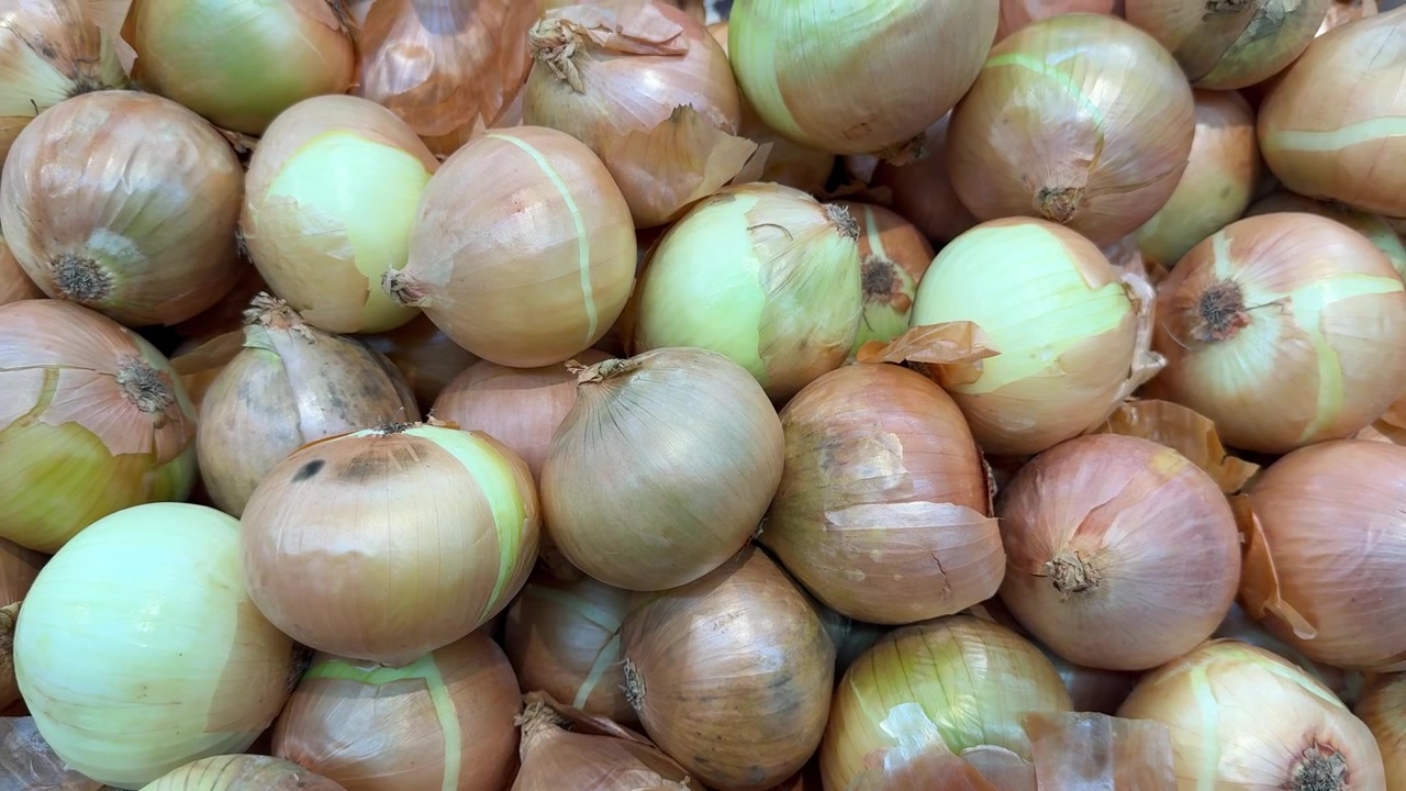 Świeże żółte cebule ułożone w stos w sklepie spożywczym.