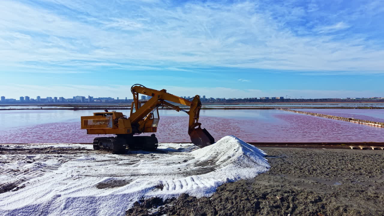 Escavatore al lavoro vicino a un lago rosa con lo skyline della città sullo sfondo durante il giorno