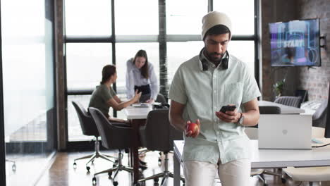 Young-Asian-business-man-with-a-beard-holds-an-apple-and-a-phone-in-an-office-setting