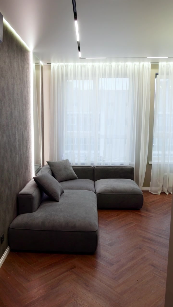 Corridoio stretto che si apre su un divano grigio, interno di un micro appartamento moderno allestito da un interior stylist, costruito