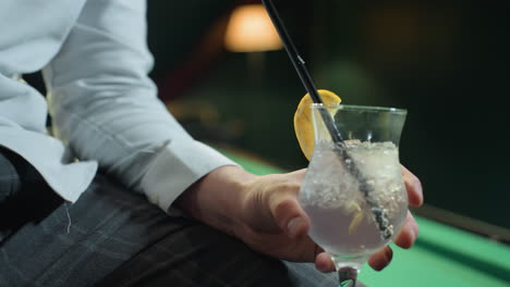 close-up of person, face not visible, wearing white shirt and grey trousers, holding glass of lemon drink with black straw. ice cubes and lemon slice add refreshing detail as camera zooms in