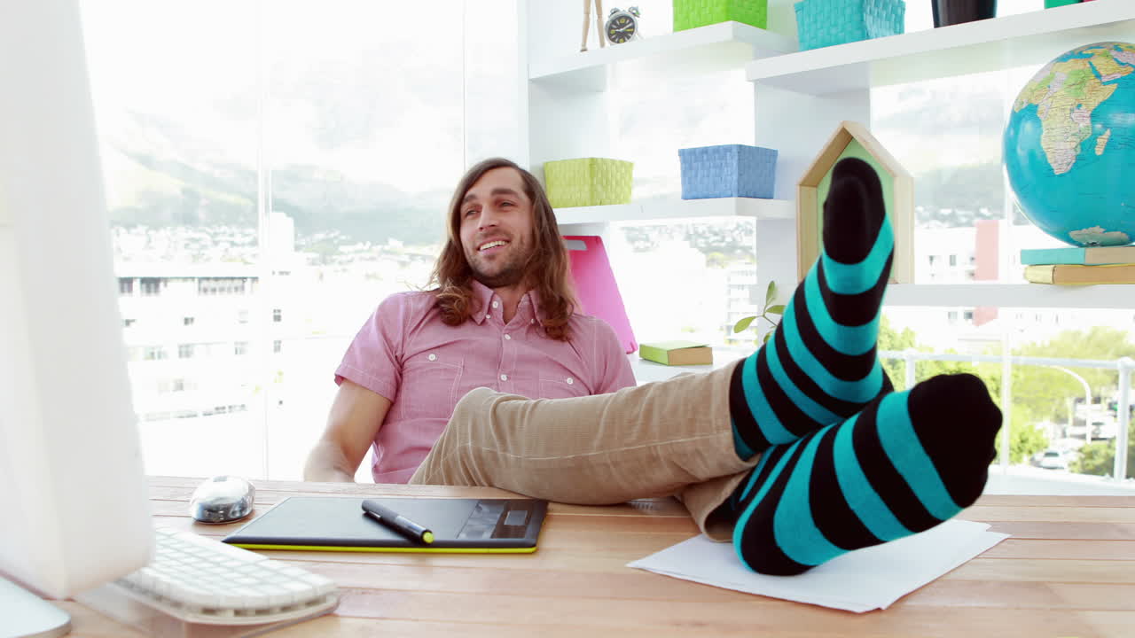 미소 짓는 그래픽 디자이너가 책상에서 휴식을 취하고 있습니다.