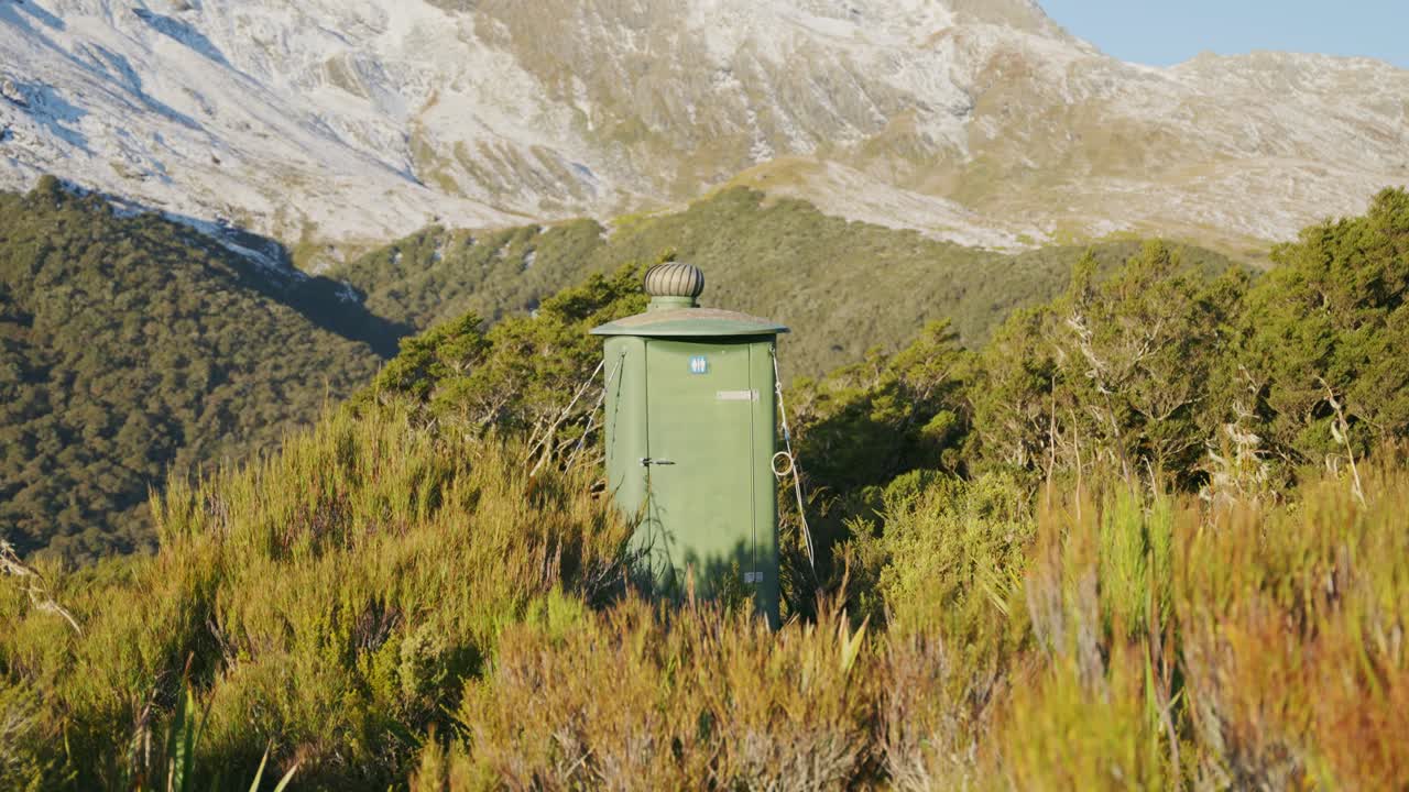 Public toilet booth located on top of mountain in natural park in New Zealand. WC bathroom for tourists and hikers climbing up mountain or track. Travel restrooms in bushes for hygienic use outdoors