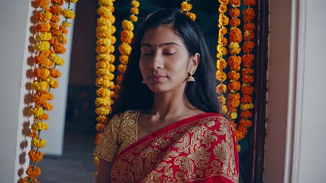 indian woman, wearing a red and gold saree, stands gracefully amidst vibrant orange and yellow marigold flower decorations, celebrating the festive occasion of navratri