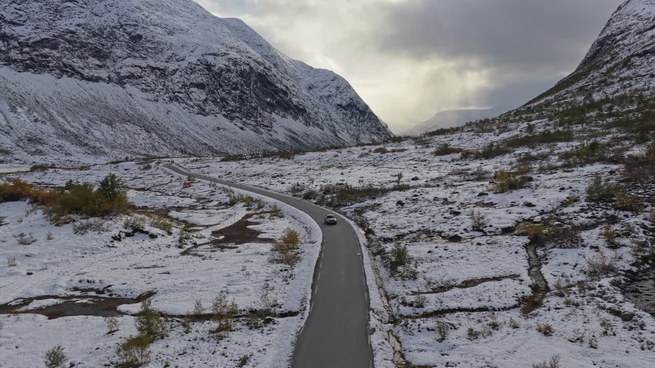 Køretøj kører mellem sneklædte bakker og bjerge i Norge.