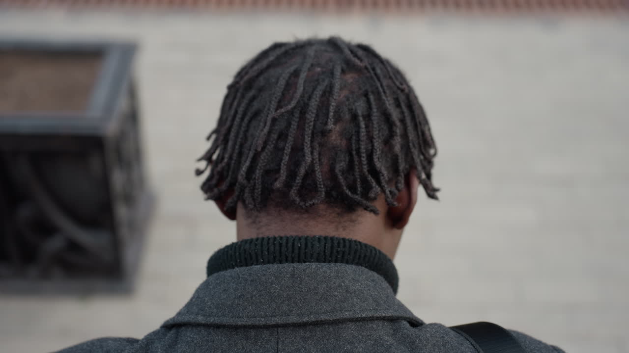 Back shot showing rough twisted natural hair on man wearing grey wool coat, emphasizing detailed texture, natural hairstyle, and cultural identity in outdoor environment with neutral background