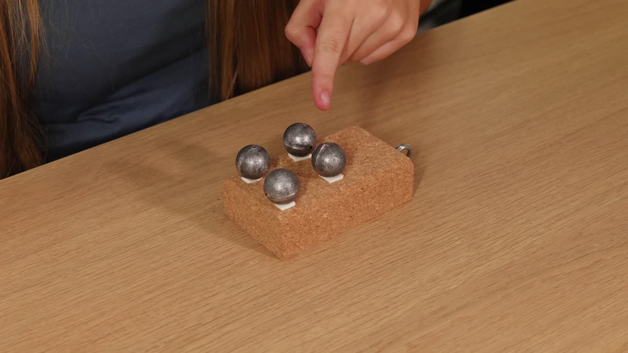A person interacts with metal spheres on a wooden block, demonstrating balance and coordination in a well-lit environment