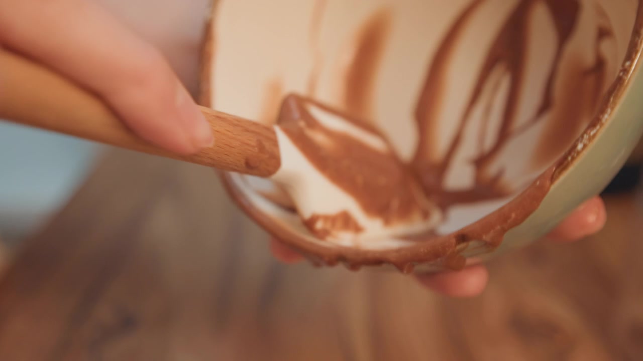Closeup of hands applying chocolate glaze smoothly. Kitchen scene showing hands preparing chocolate for dessert. Intimate kitchen moment with hands glazing dessert using chocolate and spatula