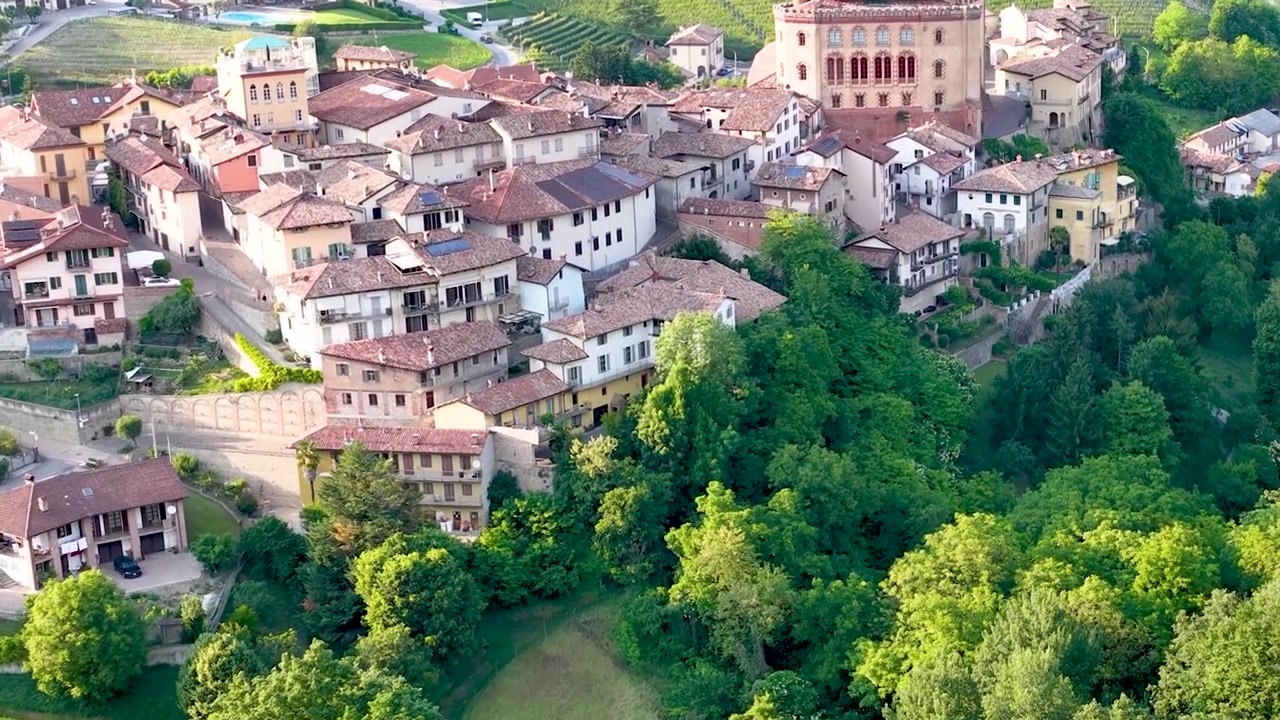 Ripresa aerea con drone si muove verso lo storico borgo di Barolo e i circostanti vigneti verdeggianti.
