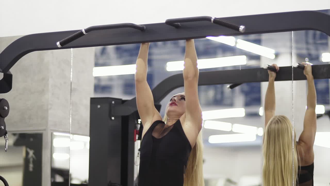 joven atlética rubia entrenando en una barra horizontal con ropa deportiva negra en el gimnasio realizando pull-ups
