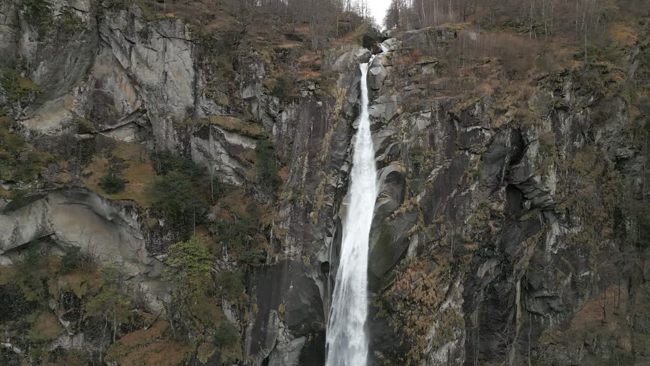 fotografía de un dron en retirada de una ligera nevada frente a una cascada de cascada de foroglio, situada en el pueblo de cavergno, en el distrito de vallemaggia, en suiza