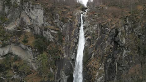 retreating drone shot of a light snowfall in front of a cascading cascata di foroglio waterfall, situated in the village of cavergno, in the district of vallemaggia, in switzerland