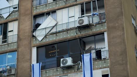 close-up, broken windows, damaged facade, israeli flags, cracked balconies, urban structure, tel aviv, aftermath scene, exterior shot