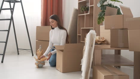 smiling woman packing bowls into cardboard box for moving