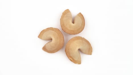 la parte superior de tres deliciosas galletas con predicción girando lentamente sobre la mesa. adivinación. aislado, sobre fondo blanco.