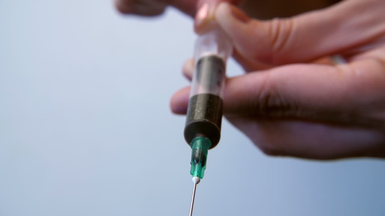Close-up of Hand Pushing Syringe Plunger Expelling Dark Liquid