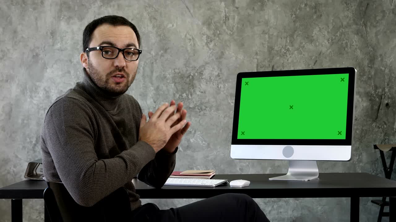 retrato de un joven guapo en casual en la oficina hablando con la cámara explicando algo cerca de la pantalla. muestra de maqueta de pantalla verde