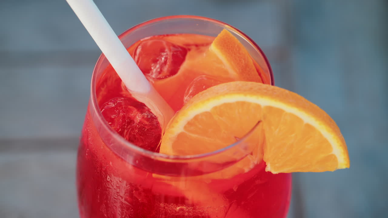 Primo piano di un cocktail rosso-arancio rinfrescante con una fetta d'arancia e cubetti di ghiaccio, scattato all'aperto in una giornata di sole a Cannes