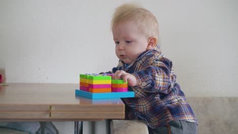 small boy plays with bright toy standing at wooden table