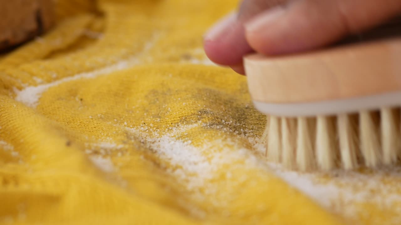 Primo piano di una mano che rimuove sale e sporco da un tessuto giallo.