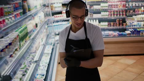 Un-Vendedor-De-Raza-Mixta-Usa-Una-Tableta-En-Un-Supermercado-Sintiéndose-Feliz-Bailando,-Escuchando-Música