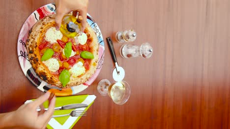 video vertical de manos vertiendo aceite de oliva en una hermosa pizza italiana fresca