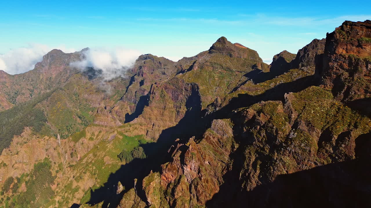 Inaccessible huge rocks with no vegetation on. White cloudscape appearing from behind the mountains. The Madeira Islands, Portugal. Aerial view.