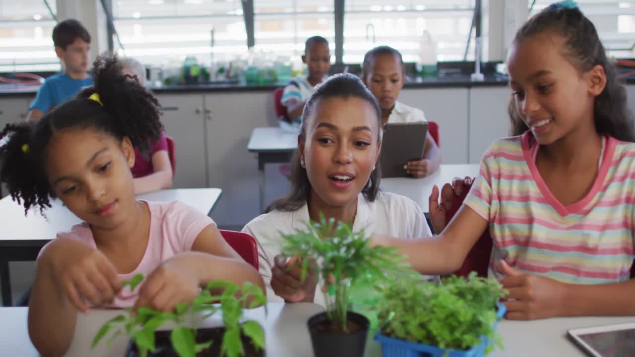 Diverse group of schoolchildren and teacher lwith plants in classroom during nature studies lesson