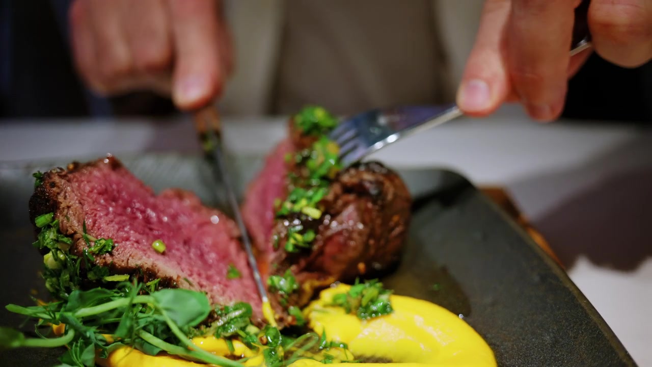 Close up of a grilled steak being sliced with a knife and fork at a restaurant