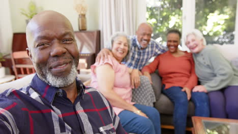 Feliz-Hombre-Afroamericano-Mayor-Tomándose-Selfie-Con-Diversos-Amigos-En-Una-Habitación-Soleada,-Cámara-Lenta