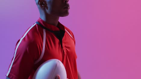 african american male rugby player with rugby ball over pink lighting