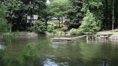 Old-dock-stretched-out-over-green-water-of-a-lake-or-a-pond-in-the-trees-in-the-south