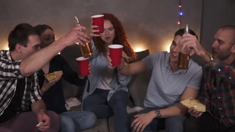 Portrait-of-diverse-group-of-friends-have-delivered-pizza-celebrating---happily-drinking-beer,-cheers.-Having-fun-party-in-cozy-room-decorated-with-garland-lights-in-a-company-of-close-friends