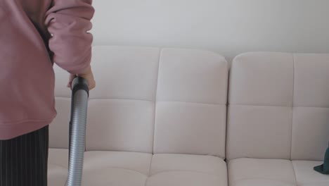 a woman vacuums a white sofa in her living room