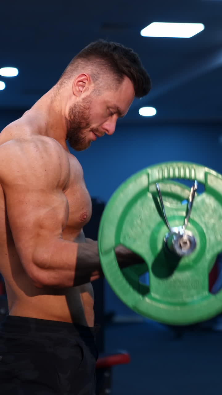 Muscular athlete doing exercise with barbell. Strong man working out arm muscles. Bodybuilding shoulder exercise in a gym. Vertical video