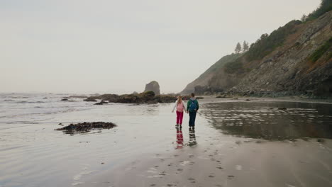 two people walking on a sandy beach towards a rocky coastline