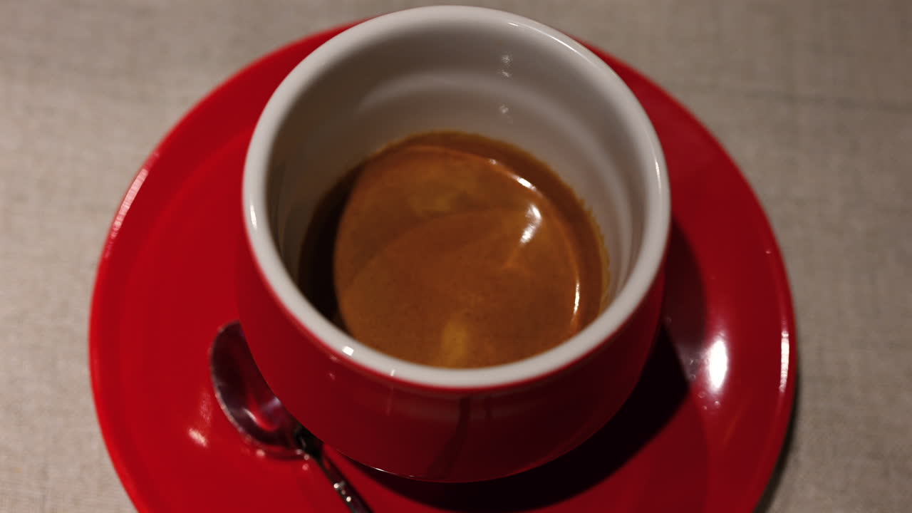Caffè espresso fresco servito in una tazza di ceramica rossa con crema in superficie, in un ambiente da bar