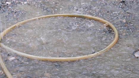 coiled hosepipe with puddles on water bogged gravel ground on a building construction worksite during a heavy, raining downpour day