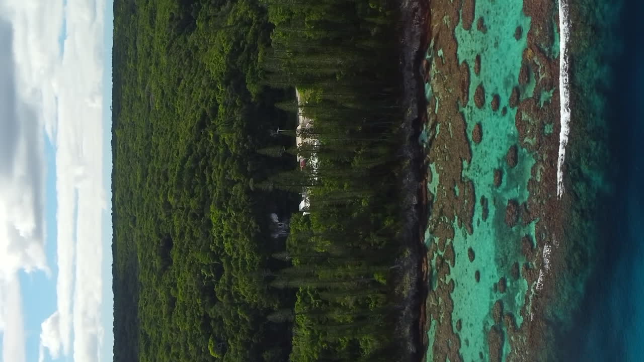 Ascending aerial shot revealing crystal turquoise water, coral reef and rugged coastline, New Caledonia