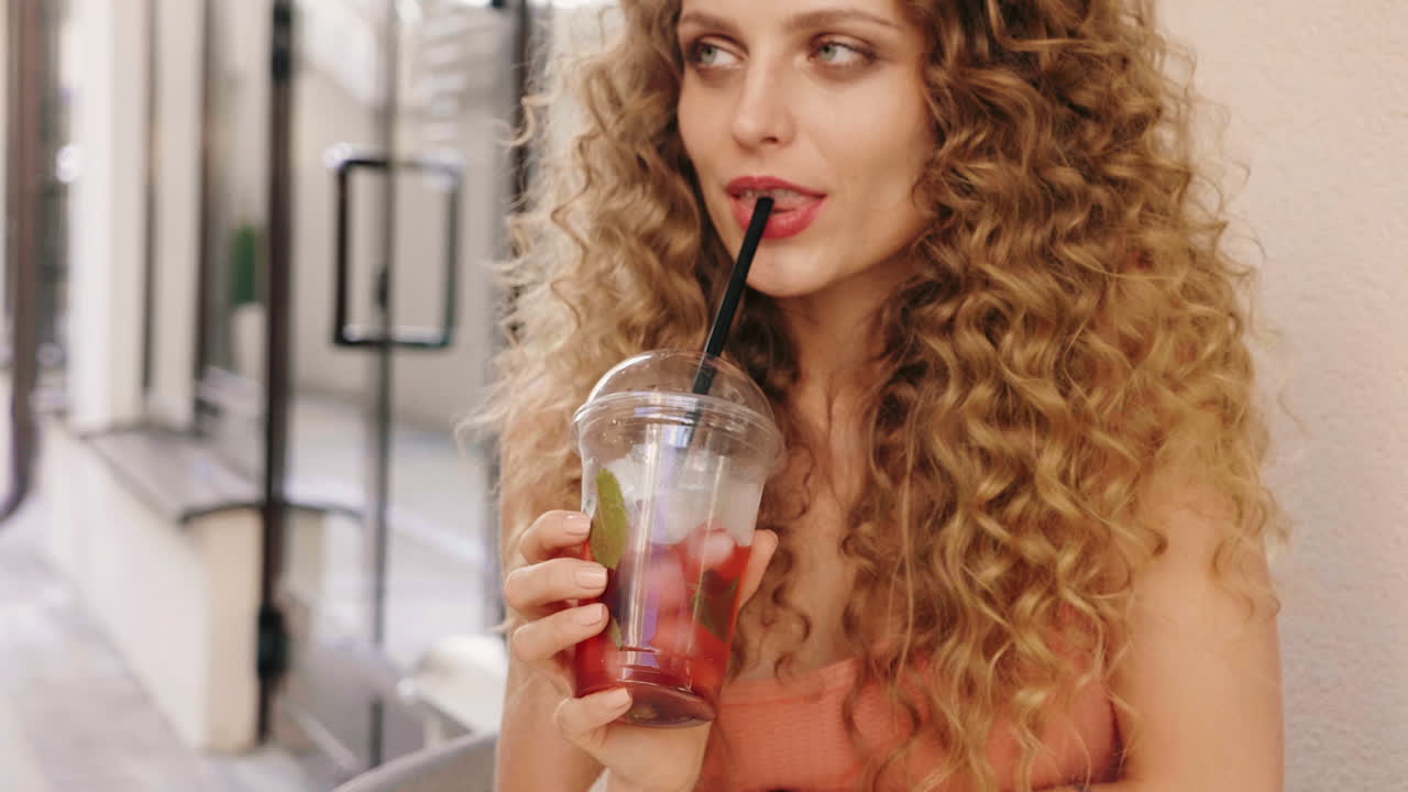 Donna con capelli ricci che si gode un drink all'aperto