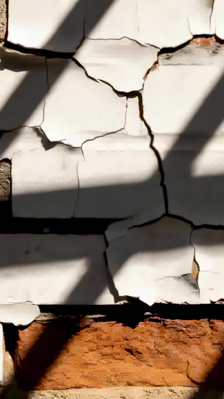 Vertical video: Sun moving casting shadows across outside peeling wall showing crack and bare brick