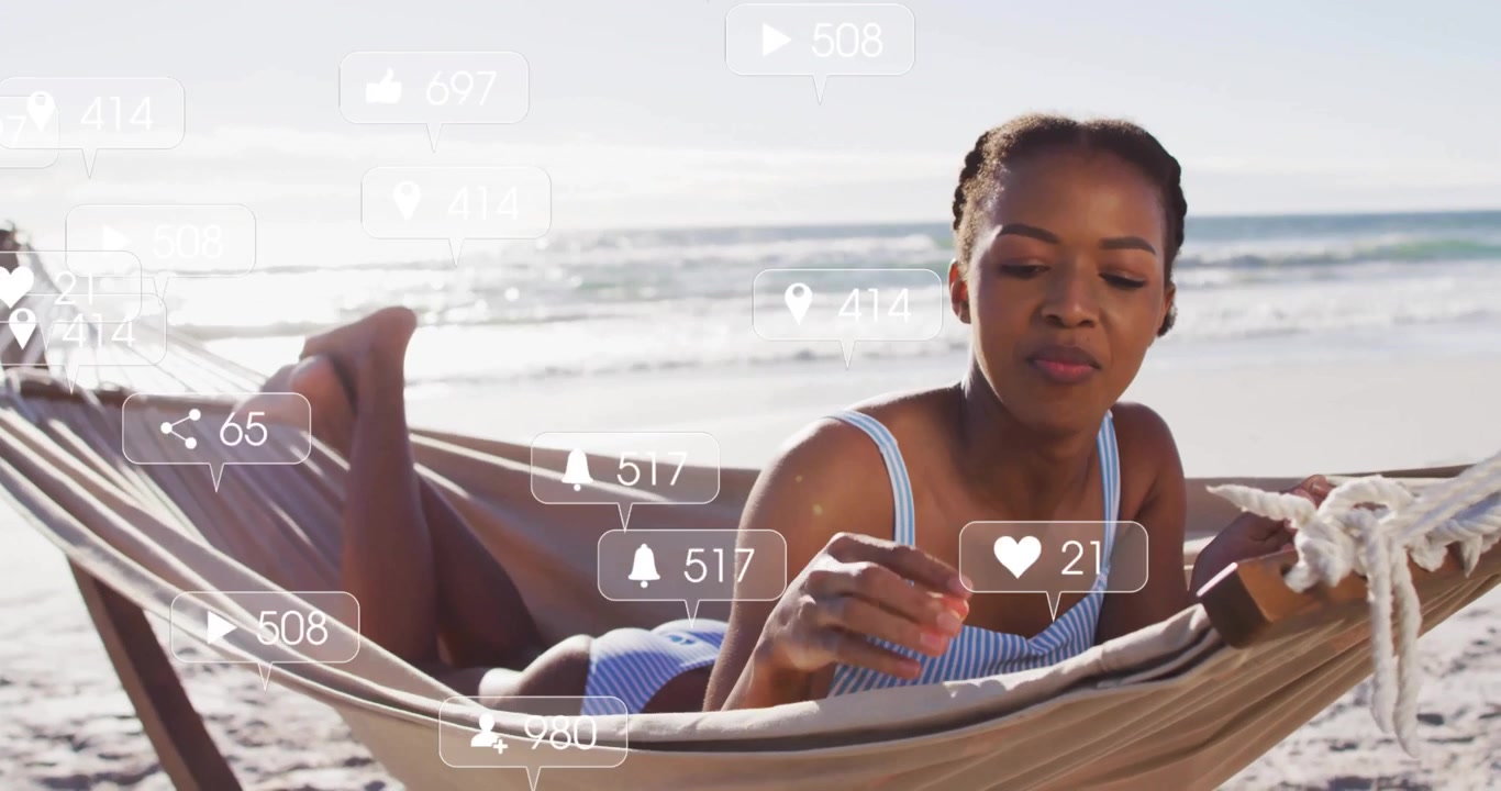 Woman powering up tablet in seaside hammock checking social stats via bubbles listening via earbud