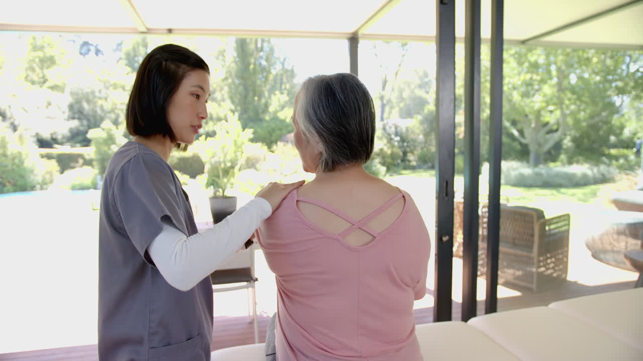 Assisting senior asian woman with shoulder exercises, physiotherapist helping at home